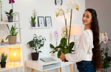 A woman holding a potted orchid plant in a bright, cozy room.