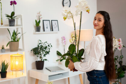 A woman holding a potted orchid plant in a bright, cozy room.