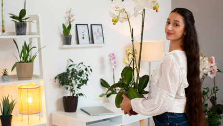 A woman holding a potted orchid plant in a bright, cozy room.