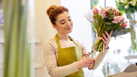 Woman arranging flowers in a bouquet with a smile.