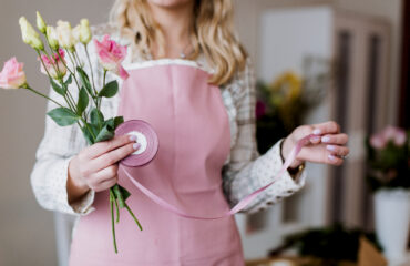 Woman holding flowers and wearing an apron with a stethoscope.