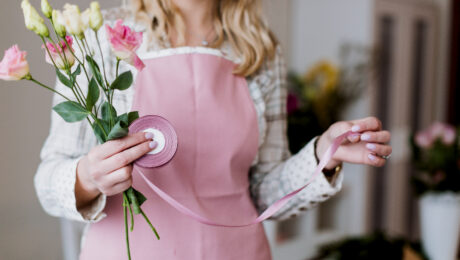 Woman holding flowers and wearing an apron with a stethoscope.