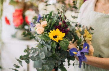A vibrant bouquet featuring a bright sunflower among mixed flowers and greenery.