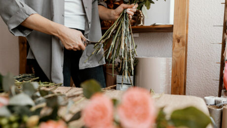 Person trimming stems of flowers with scissors indoors.