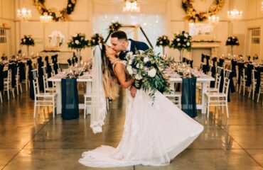 Bride and groom sharing a romantic dip kiss in a decorated wedding hall.