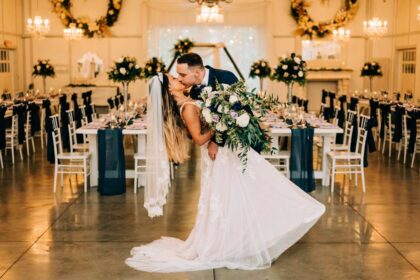 Bride and groom sharing a romantic dip kiss in a decorated wedding hall.