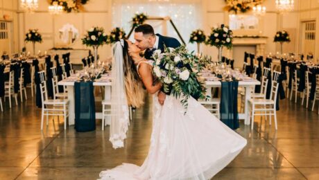 Bride and groom sharing a romantic dip kiss in a decorated wedding hall.