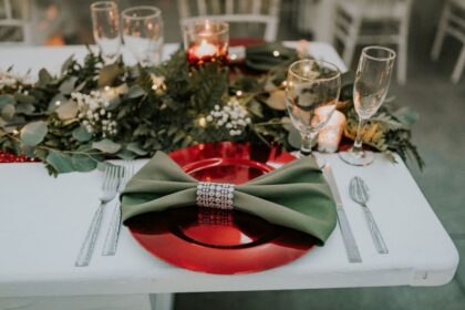 Elegant holiday table setting with green napkin and red plate.